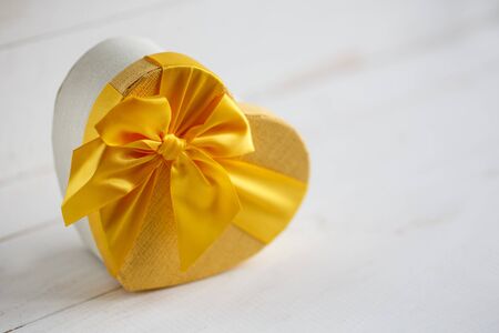 Closed heart shaped gift box on white background, copy space. Gift decor with yellow bowの写真素材