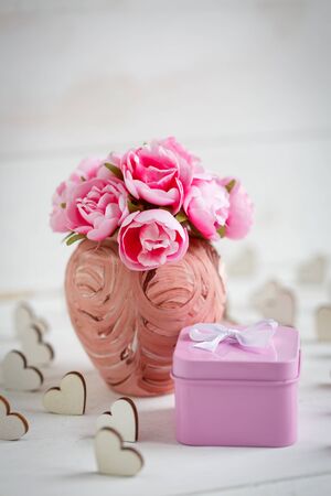 Decorative wooden hearts, vase with flowers and gift box on white textured wooden table. Concept of love, celebration and gift.の写真素材