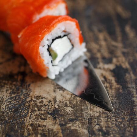 Philadelphia sushi roll with sushi knife on wooden background. Sushi menu. Japanese cuisine.の写真素材