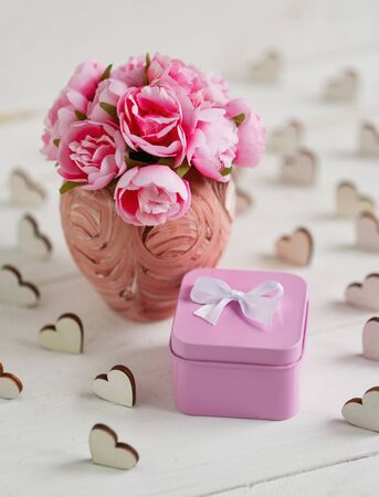 Beautiful composition with small square metallic pink gift box and delicate roses in pink vase on white wooden backgroundの写真素材