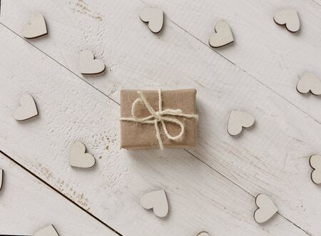 Small gift wrapped in pink paper, decorative hearts around the gift on white background.の写真素材