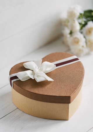 Beautiful brown gift box in the form of heart with a bouquet of flowers on the backgroundの写真素材