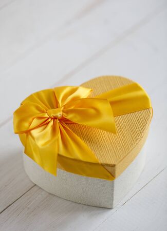 Yellow gift box in the form of heart on a white wooden backgroundの写真素材