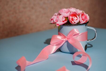 Beautiful little roses in a blue metal retro cup. Decor with pink ribbon. Mother's day. Women's day. Valentine's day, Birthday greeting concept background.の写真素材