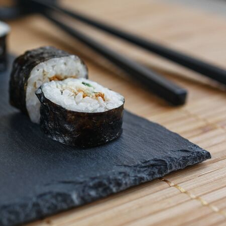 Maki sushi, two pieces of tuna and cucumber on a black board. Black sticks on the background. Macro shot of Japanese foodの写真素材