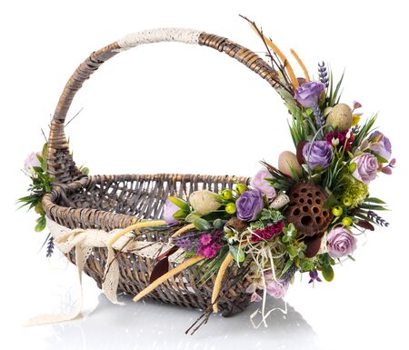 Brown wicker basket with original handle. Decor with flowers, eggs and ribbons. Made for Easter celebration. Isolated on a white backgroundの写真素材
