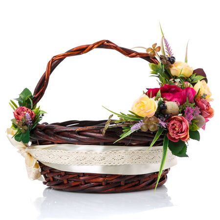 Dark brown wicker basket with original handle and floral decoration on a white background. Decor of yellow and pink flowers, green. wide ribbon and lace. Side view.の写真素材