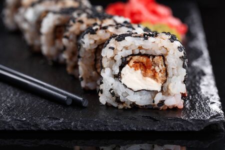 Closeup of sushi roll with cream cheese and fish. Sushi on stone dark plate on black background. Japanese food.の写真素材