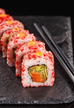 Uramaki sushi rolls covered in red caviar filled with salmon and cucumber. Served on a black stone board. Japanese food.の写真素材