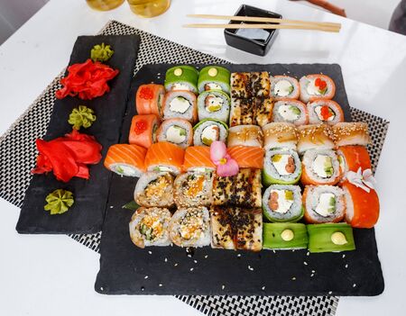 Set of sushi. Different types of Maki and Nigiri sushi with ginger and wasabi sauce. Bright and colorful service at the restaurant. Served on dark stone sushi boards. Huge sushi set.の写真素材