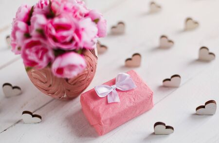 Vintage background with hearts, gift box and bouquet of pink roses in vase on white wooden board. Holiday and love conceptの写真素材