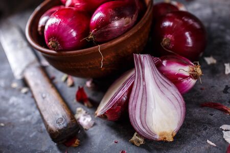 Red onion in wooden bowl and four kitchen knife on dark gray background. Cut the bulb in half on the table. Close up.の写真素材