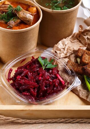 Ukrainian traditional borscht and vegetable broth in paper cups, beet salad in a glass bowl, bread crumbs and green onions on a rustic wooden tray. Ukrainian dishes. Ukrainian menu.の写真素材