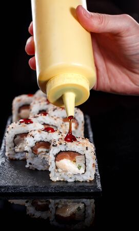 Delicious sushi roll served on black slate. In the frame, the hand of a chef pouring food with sweet sauce. Japanese food.の写真素材