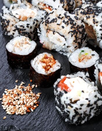 Background with different sushi rolls on a black board with a handful of sesame seeds. Traditional sushi. Delicious Japanese food.の写真素材