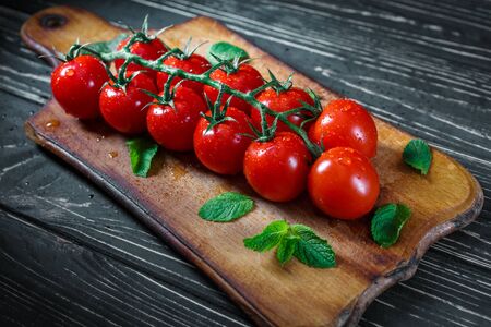 Tomatoes on a branch. Tomatoes on a beautiful green branch in drops of water with mint leaves on a wooden kitchen board. Ingredients for cooking.の写真素材