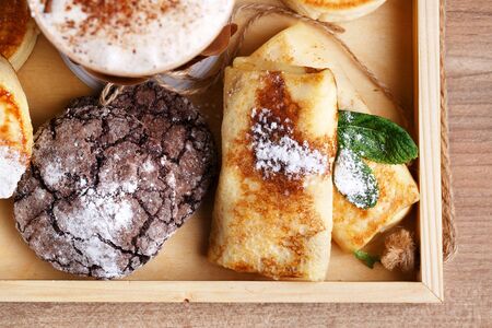 Cinnamon coffee in a disposable paper cup with a blank white card for the inscription. Cookies and apple strudel on a brown wooden tray.の写真素材