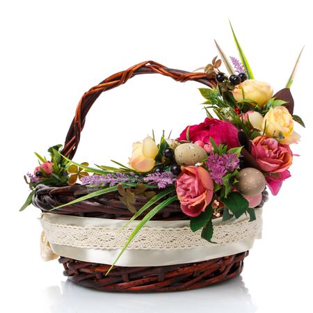 Dark brown wicker basket with original handle and floral decoration on a white background. Decor of yellow and pink flowers, green. wide ribbon and lace. Side view.の写真素材