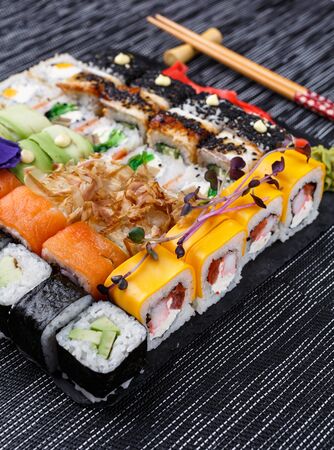 Sushi roll japanese food in restaurant on a stone board. Diferent Sushi roll set with different fish, vegetables, cheese, sesame, ginger and wasabi close up. Wooden sticks on gray background. Top viewの写真素材