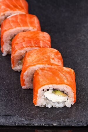Philadelphia sushi rolls with salmon and cream cheese and avocado on a black slate plate close up. Traditional Japanese food.の写真素材