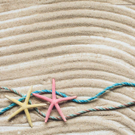 Holiday summer background. Colored starfish on sandy beach. Wavy sand texture. Top view with copy space.の写真素材