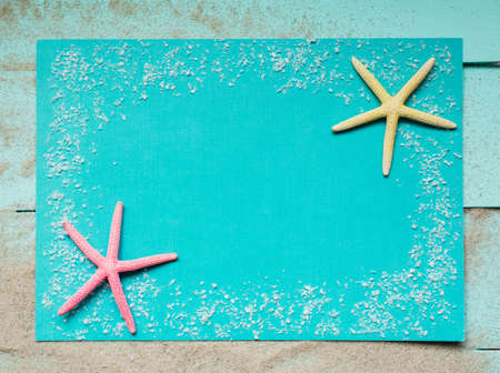 Two colored starfish and sea salt on a turquoise background. Natural material frame with place for...