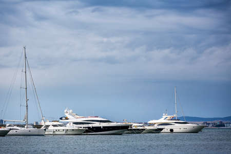 Several luxury white boats on water with reflections standing on pear in sea port