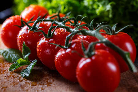 Ripe red fresh tomatoes on the vine. Lettuce and mint leaves. Tomatoes with drops of dew.の写真素材