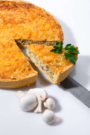 Taking of delicious mushroom pie with a kitchen spatula. Fragrant vegetable pie on white table with ingredients for cooking.の写真素材