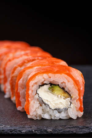 Beautiful sushi roll topped with salmon stuffed with cream cheese on a black stone board. Sushi menus.の写真素材