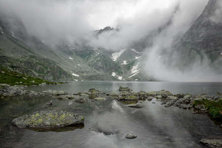 Hincovo pleso in the fog between the mountains. High Tatras of Slovakia. Mountain lake and mountains are covered with fog.の写真素材