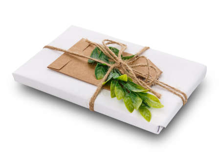 Decorated gift with green branch, burlap ribbon, greeting tag and wrapped in white paper. Isolated on white backgroundの写真素材