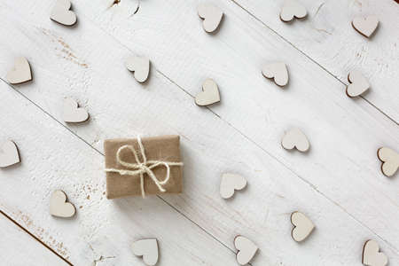 Handmade gift in kraft paper on a white background. Wooden decorative hearts around gift. Valentine or other holiday.の写真素材