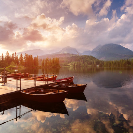 View of a mountain lake Strbske pleso in the High Tatras. Slovakia. Boats on the water glow in the sun at sunset.の写真素材