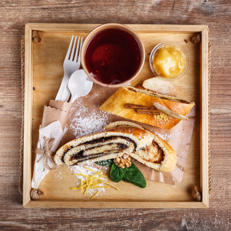 Poppy and apple strudel on a wooden rustic tray. Tea in a paper cup with a blank white space for...