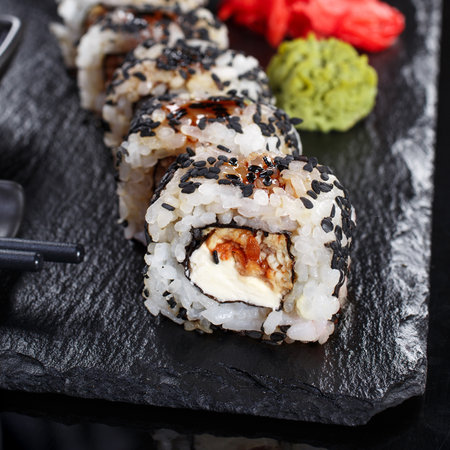 Japanese Traditional Cuisine. Sushi roll with sesame seeds is served with chopsticks and soy sauce on black slate, decorated with wasabi and ginger. Mockup of sushi menu, close up.の写真素材