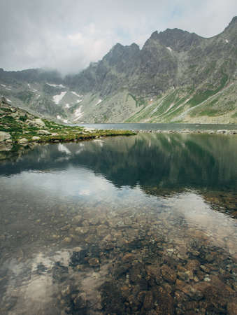 Wonderful foggy sunrise over a lake in the mountains. Hincovo pleso in the fog during sunrise. Picturesque landscape of crystal clear lake against the background of mountains in the fog.の写真素材