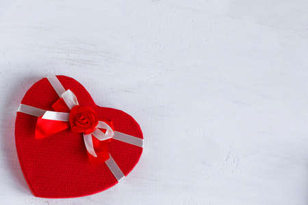 Red gift box in the shape of a heart with ribbon on a white wooden background. Place for text.の写真素材