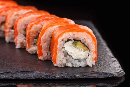 Sushi roll with salmon, avocado and cheese laid out on a black plate. Sushi menu. Japanese food.の写真素材