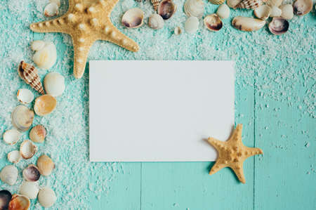 Summer template with greeting card. Little seashells, starfish and sea salt on a turquoise wooden background. Place for text on white blank card. Travel concept, flat lay, top view.の写真素材