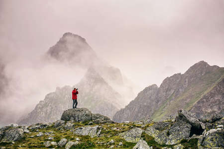 Hiker with camera standing on top of a mountain and enjoying landscape. High Tatras mountains. Landscape photographer photographs a mountain view.の写真素材