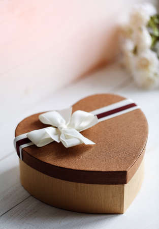 Beautiful brown gift box in the form of heart with a bouquet of flowers on the background.の写真素材