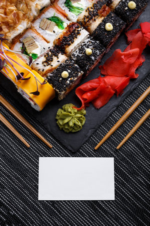 Assorted sushi set on stone background. Huge set of rolls with different stuffing. Salmon, tuna, eel, avocado, cucumber, Philadelphia cheese, cutlets and caviar. Blank white card for inscriptionの写真素材