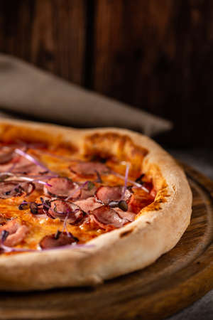 Italian pizza with meat, cheese and basil close up. Dish on a wooden background.の写真素材
