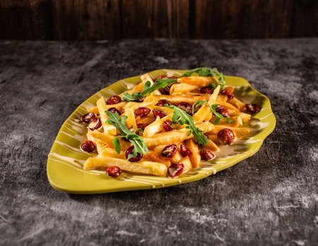 Hearty lunch of french fries, sausages and arugula. Dish in a yellow plate on a gray concrete table. The concept of nutritious food.の写真素材