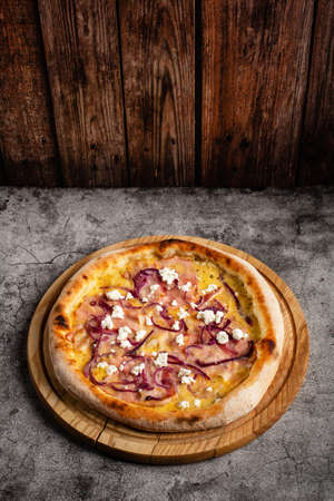 Pizza with ham, cheese and cottage cheese lies on a wooden board on a gray concrete table.の写真素材