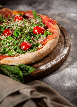 Pizza close up with arugula, prosciutto and cherry tomatoes on a wooden board. Photo for the menu.の写真素材