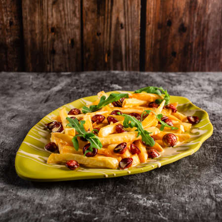 French fries with fried pieces of sausage, arugula and sauce in a yellow plate on a gray concrete table. Top view.の写真素材