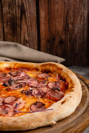 Italian pizza with meat, cheese and basil close up. Dish on a wooden background. The concept of nutritious food.の写真素材