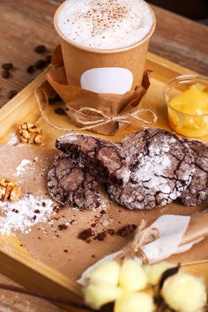 Fragrant coffee in a paper cup with foam and cinnamon and delicious cookies on a wooden tray. Place for text. Advertising banner.の写真素材